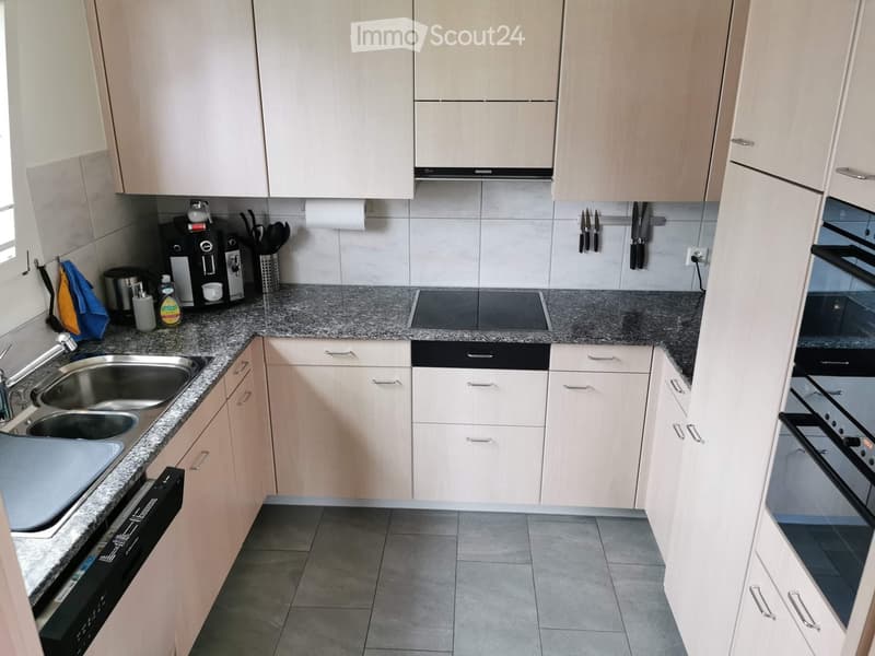 Modern kitchen with light wood cabinets, granite countertops, stainless steel sink, coffee maker, and built-in oven.