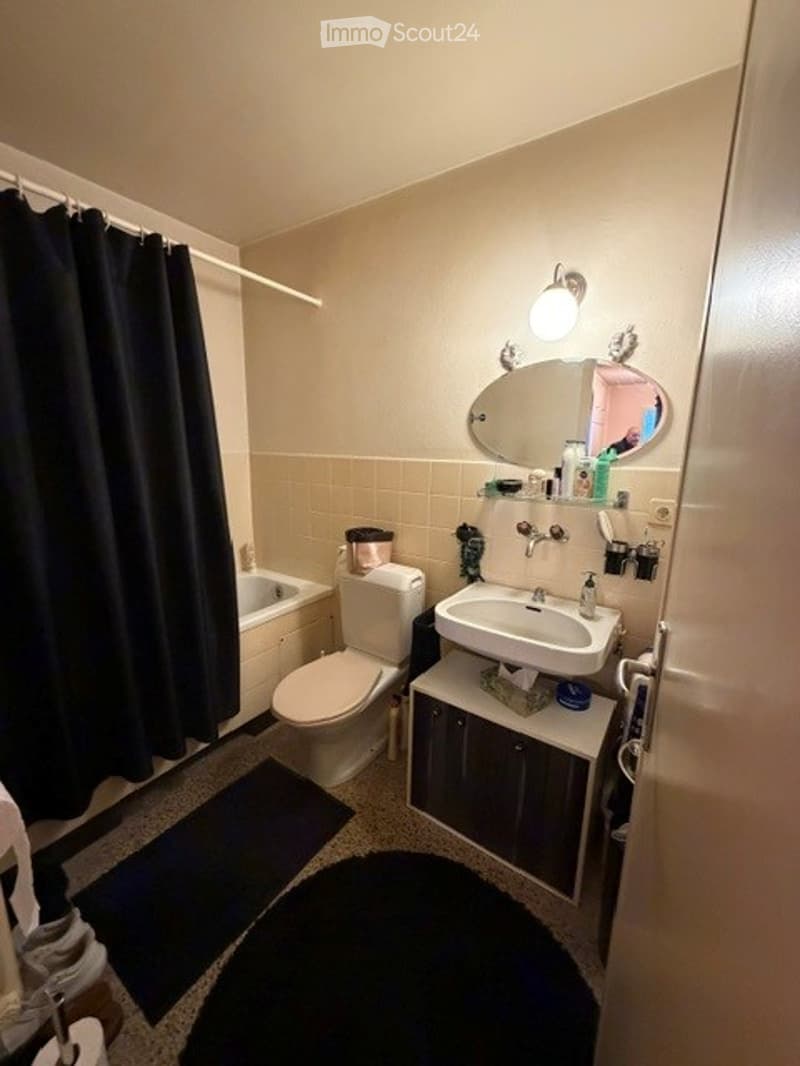 Bathroom with a toilet, sink, bathtub, mirror, dark curtain, and a small cabinet under the sink.