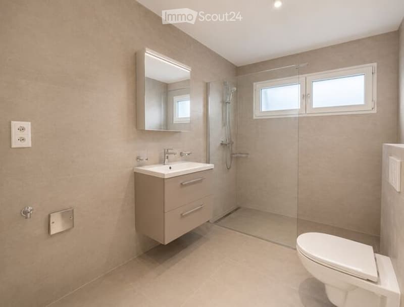 Modern bathroom with beige tiles, a floating vanity with a sink, a large mirror, a glass-enclosed shower, and a toilet.