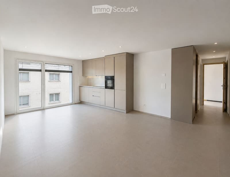 Empty room with tiled floor, white walls, and a small kitchen area featuring cabinets and an oven. Large sliding glass doors lead to a balcony.