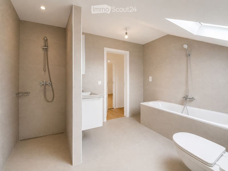 Modern bathroom with beige tiles, a bathtub, toilet, sink, and showerhead. Features include a skylight, recessed lighting, and a small shelf.