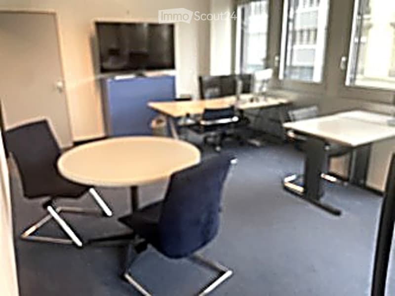 Office space with desks, chairs, a screen, and a small round table.