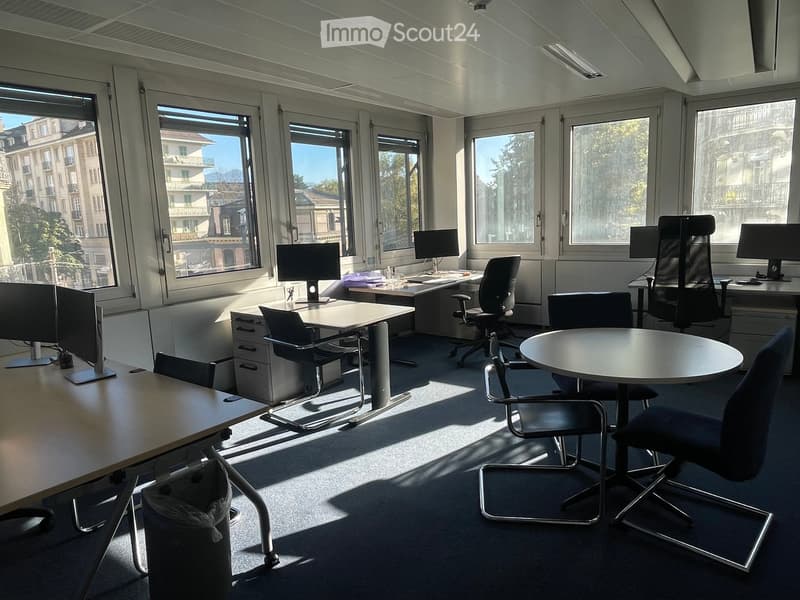 Bright office space with large windows, desks, chairs, and computer monitors arranged for multiple workstations.
