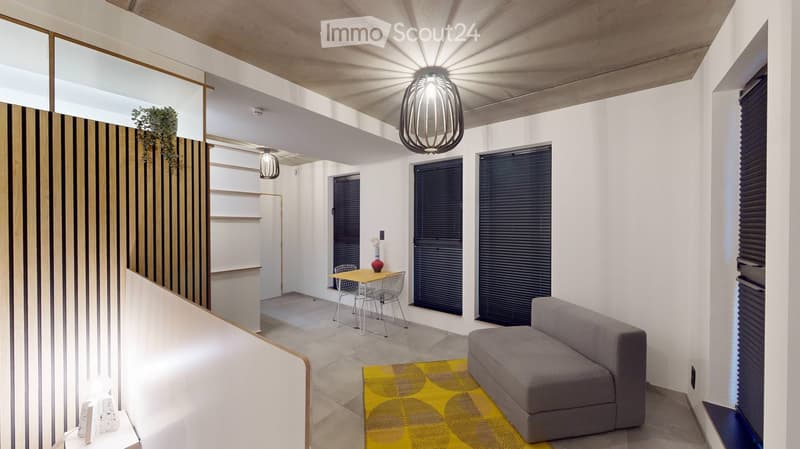 Modern living room with a grey sofa, yellow rug, small dining table with chairs, pendant lights, and a decorative vase on a shelf.