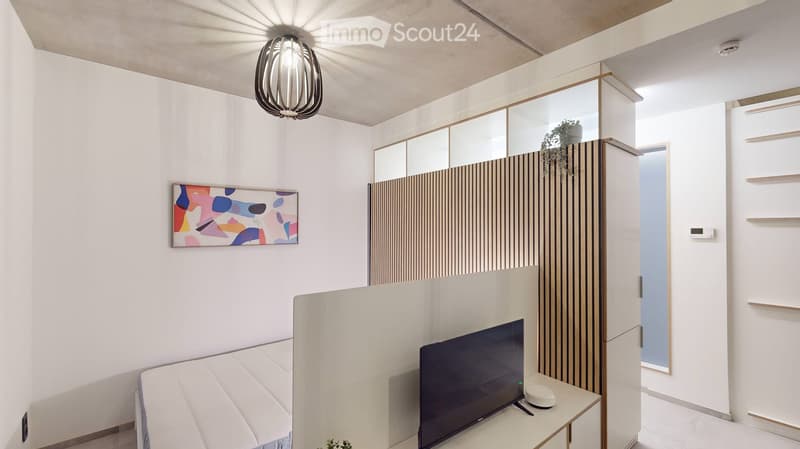 Modern, minimalist living room with a white sofa, a small table holding a TV, a large mirror, and a stylish pendant light.