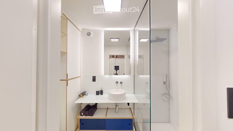 Modern bathroom with a white sink, glass shower enclosure, and a sleek cabinet with blue drawers.