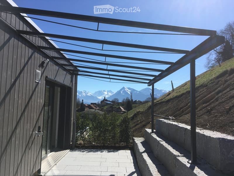 A modern covered balcony with metal framework, overlooking a scenic mountain view and a small town below.