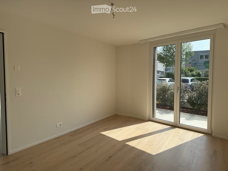 Empty room with light wooden flooring, white walls, and large sliding glass doors leading to an outdoor area.