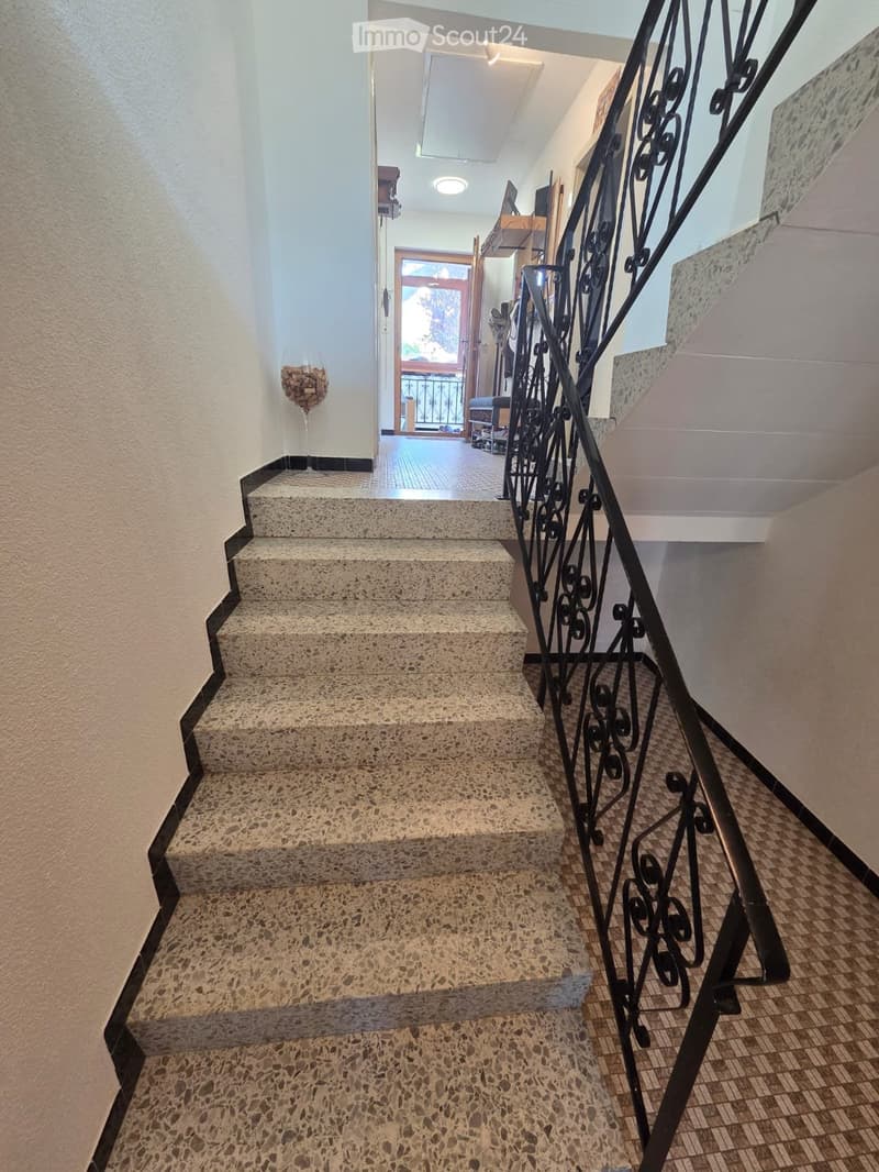Staircase with decorative wrought iron railing, leading to an open area with a glass door and balcony view.