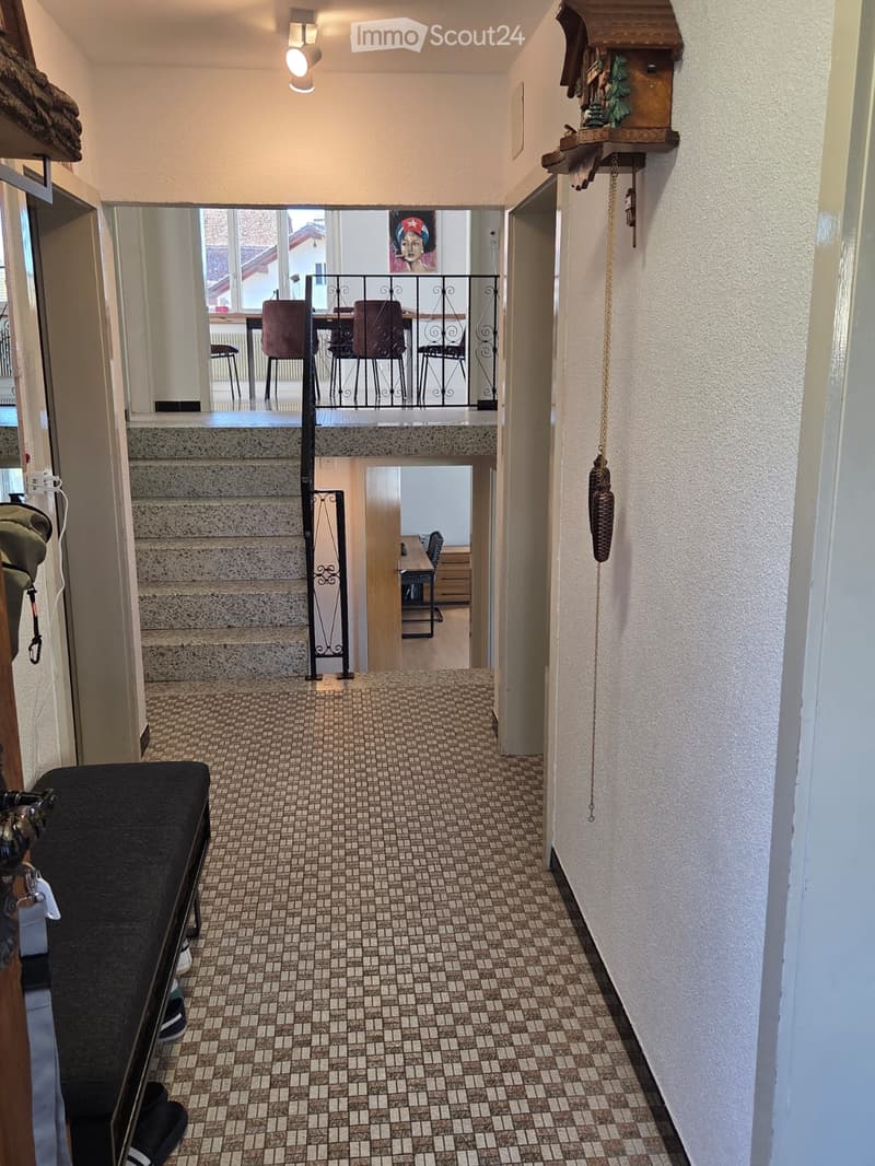 Hallway with tiled floor, staircase leading to an upper level, and a small seating area visible on the left side.
