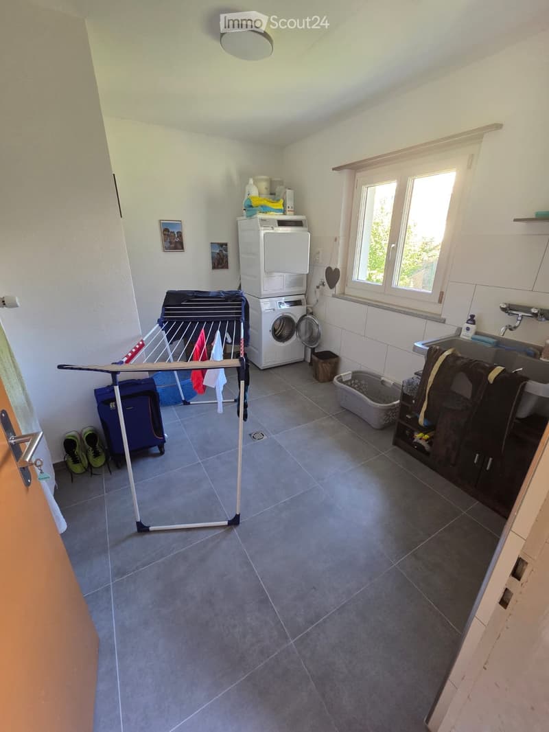 Laundry room with a washing machine, drying rack, sink, and various items including a pet carrier and shoes.