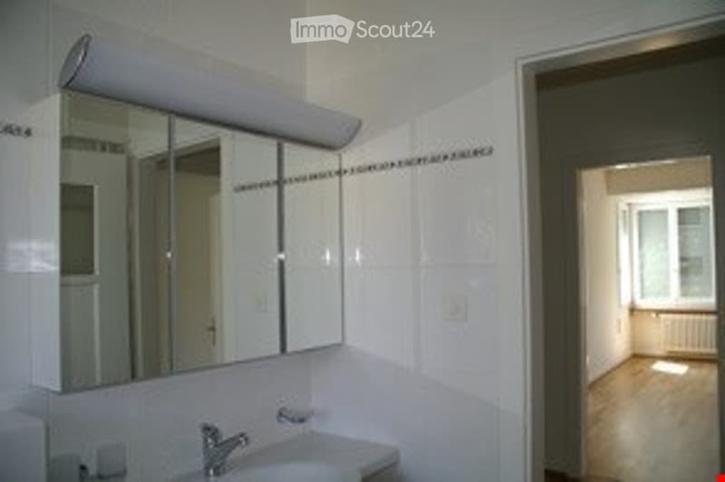 Bathroom with white tiled walls, a large mirror cabinet above the sink, and a visible doorway leading to another room.