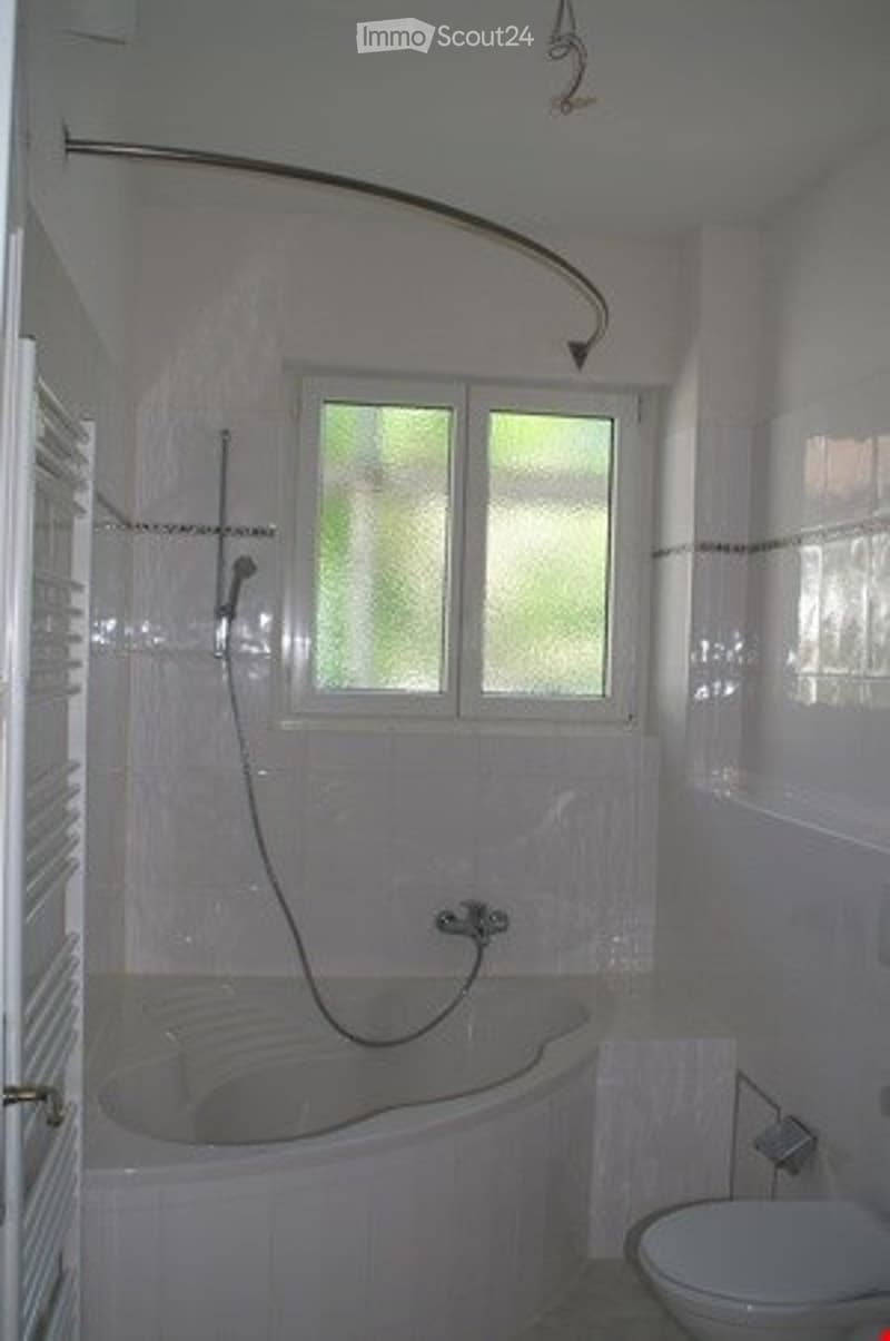 Bathroom with a bathtub, toilet, showerhead, and window. The walls are tiled in white with decorative borders.
