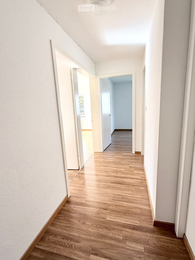 Empty hallway with wooden flooring, white walls, and open doors leading to other rooms.