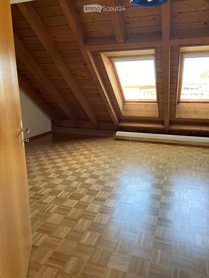 Empty attic room with wooden walls, herringbone-patterned wooden flooring, skylight windows, and a white bench along the wall.