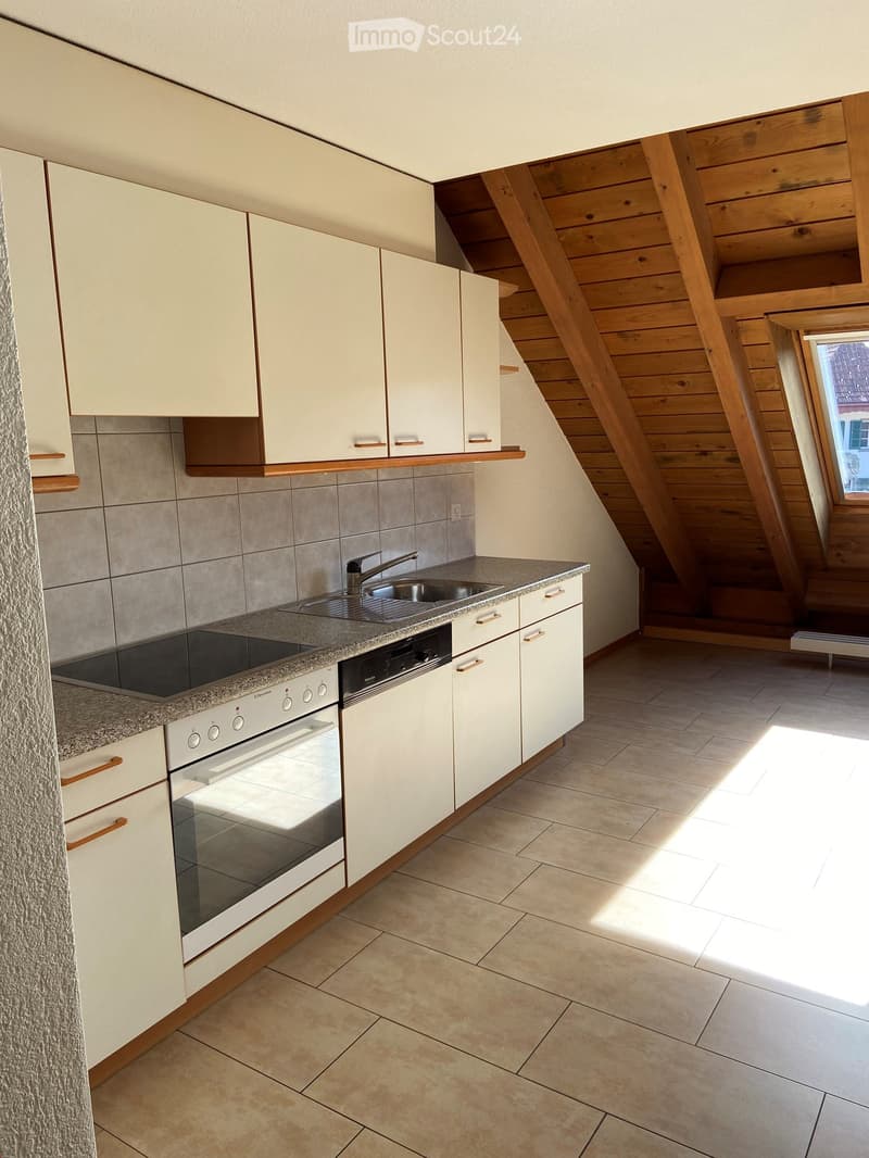 Modern kitchen with white cabinets, granite countertop, built-in oven, dishwasher, and sink. Wooden slanted ceiling and tiled floor.
