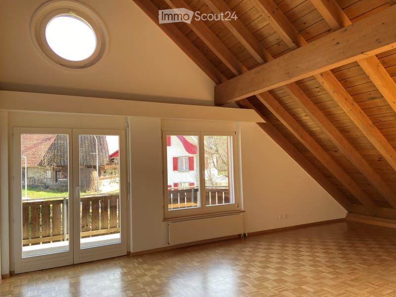 Bright, empty attic room with wooden slanted ceilings, large skylight, double doors leading to a balcony, and wooden flooring.