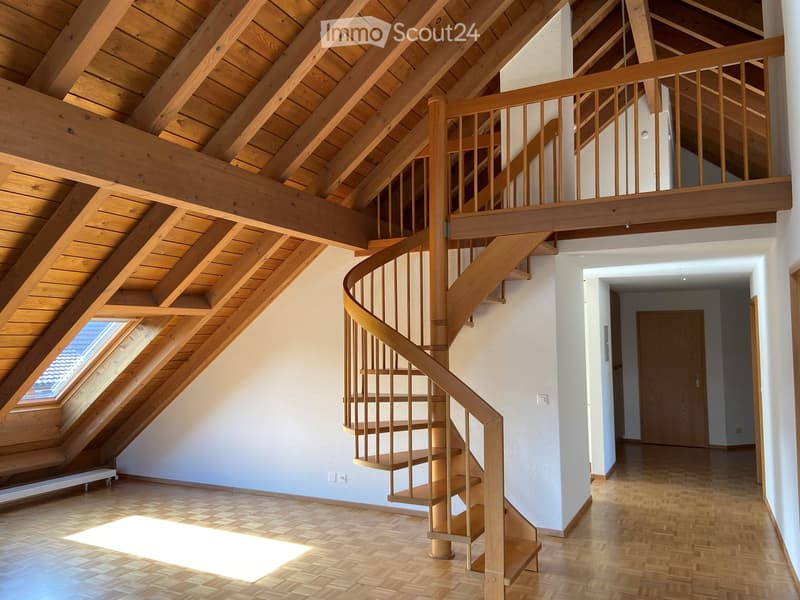 Spacious hallway with wooden flooring, a curved wooden staircase leading to an upper level, exposed wooden beams on the ceiling, and a skylight window providing natural light.