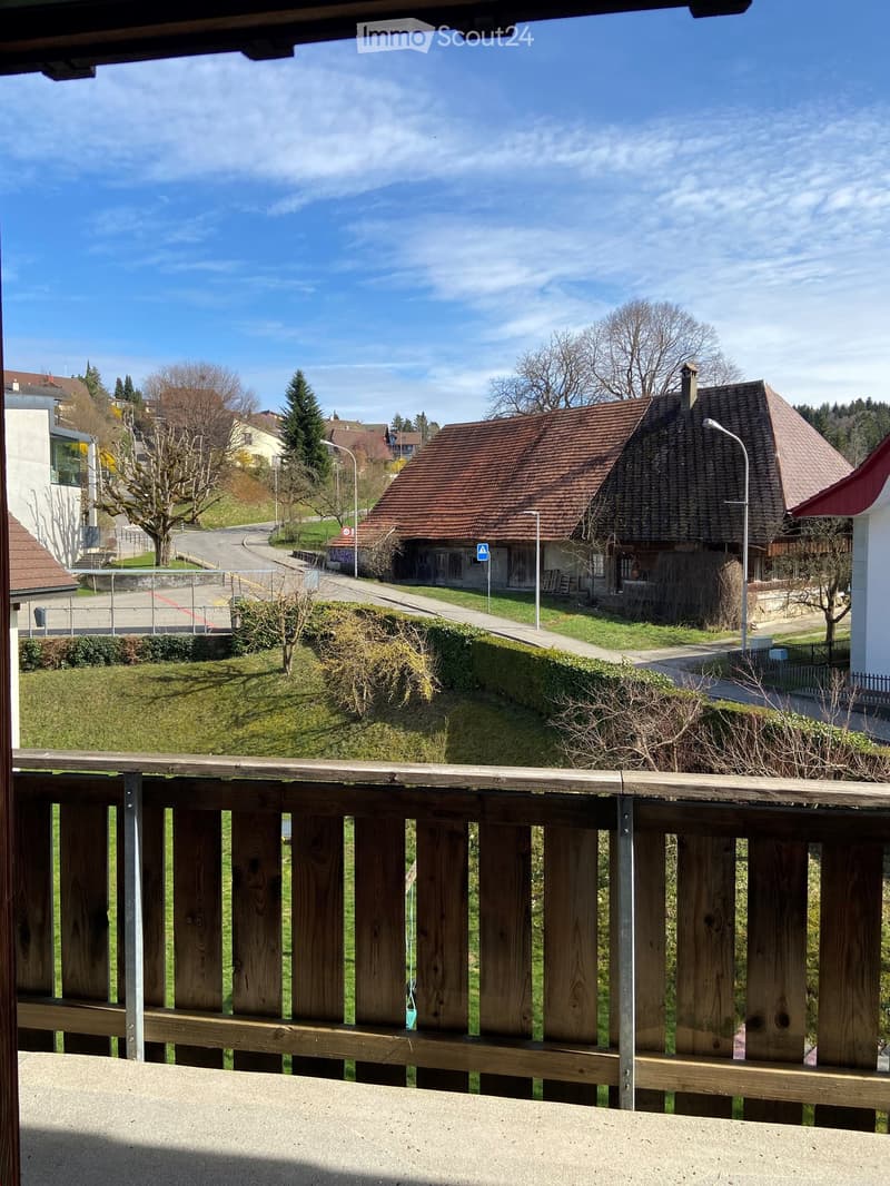 Balcony overlooking a rural village with houses, trees, and a clear blue sky.