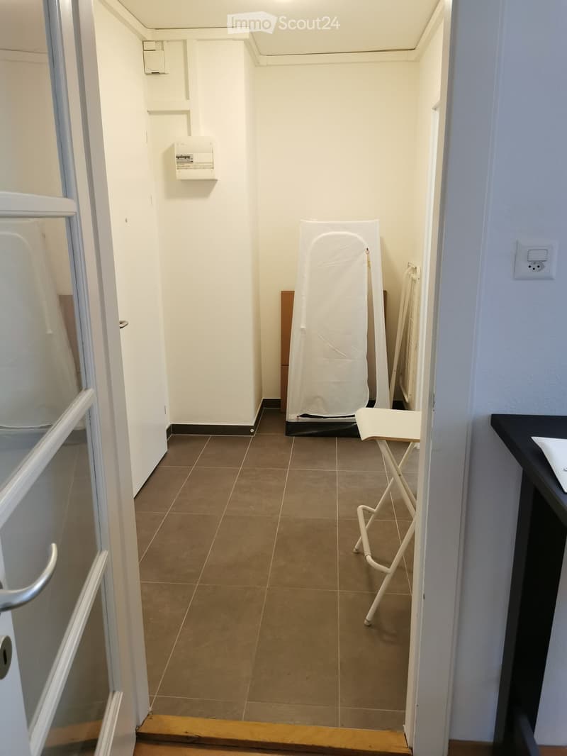 Empty hallway with tiled floor, white walls, and a small closet area with a clothes drying rack and a folded towel. No furniture or equipment present.