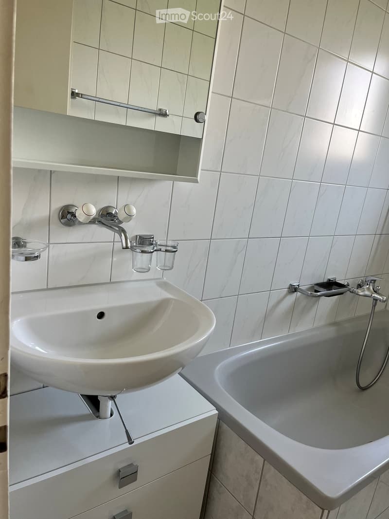 Modern bathroom with a white sink, bathtub, mirror, and modern faucet. The sink has a sleek design with a built-in cabinet below.
