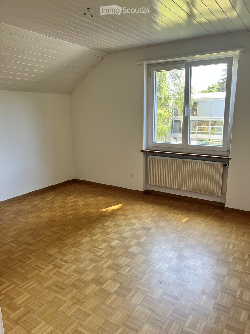 Empty room with wooden herringbone flooring, white walls, large window with radiator below, and visible electrical outlet.