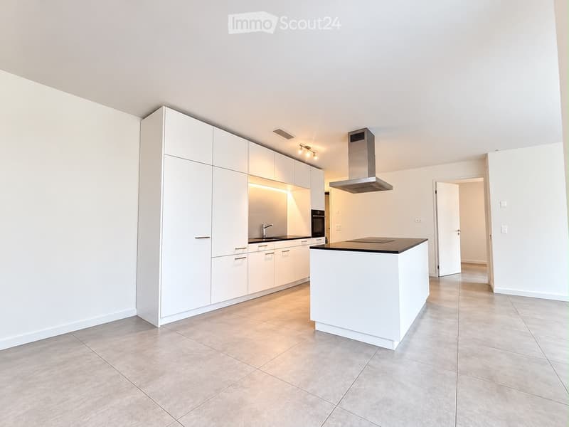 Modern, minimalist kitchen with white cabinets, a central island, and built-in appliances including a stove and oven. The space features sleek, contemporary design with a neutral color palette and ample natural light.