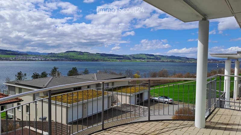 Balcony with a view of a lake and surrounding landscape, featuring a metal railing and tiled floor.