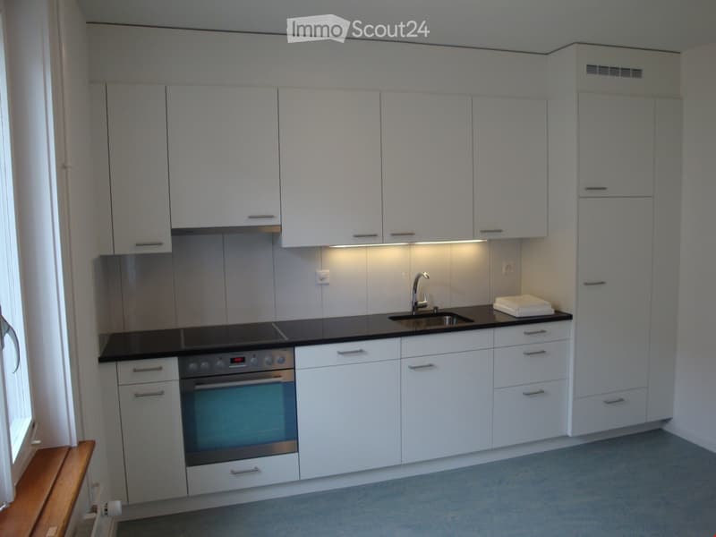 Modern kitchen with white cabinets, black countertop, stainless steel oven, sink, and faucet. Features built-in lighting and a small towel on the counter.
