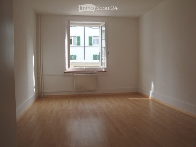 Empty room with wooden flooring, white walls, and a large window with a radiator below it.