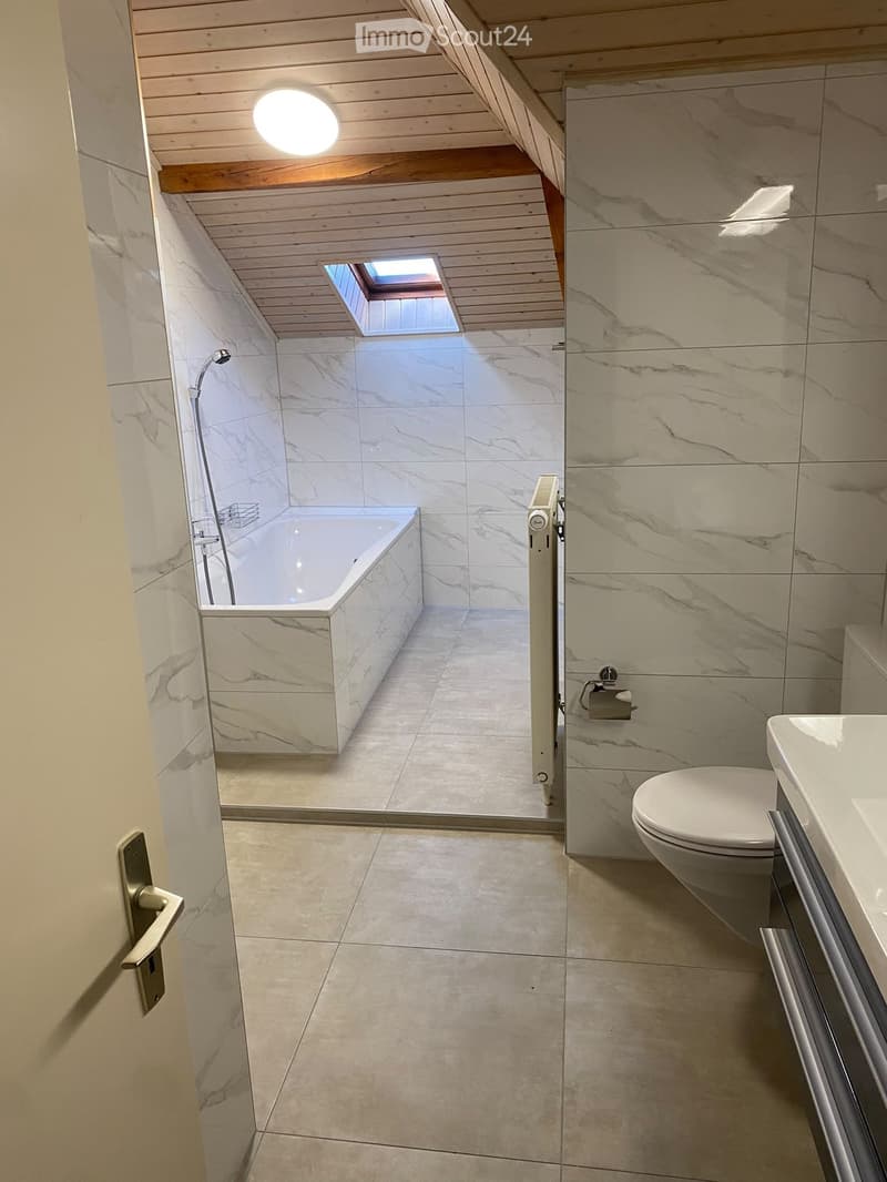 Modern bathroom with marble tiles, a bathtub, toilet, and a skylight above the bathtub area.