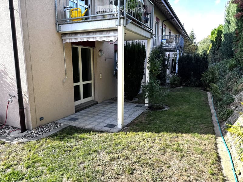 Garden area with grass, tiled patio, and balcony with outdoor furniture.