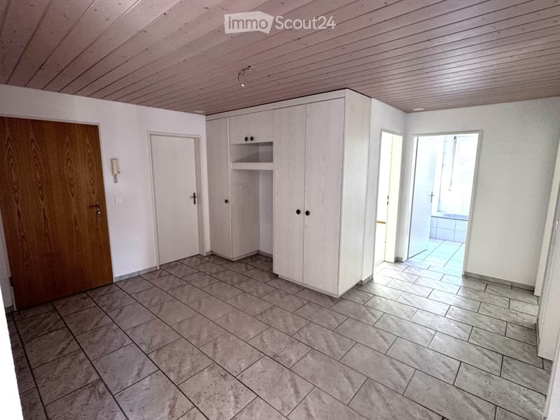 Empty room with white walls, tiled floor, wooden door, built-in white cabinet, and a view into an adjacent tiled area.