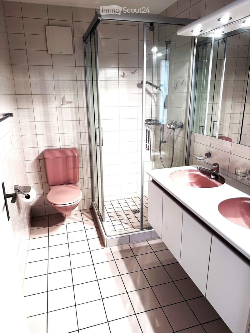 Modern bathroom with pink toilet, white sink, glass shower enclosure, and tiled walls and floor.