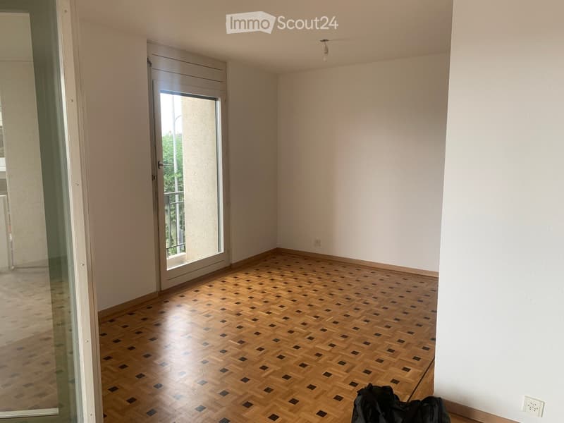 Empty room with wooden herringbone flooring, white walls, and a large glass door leading to a balcony.