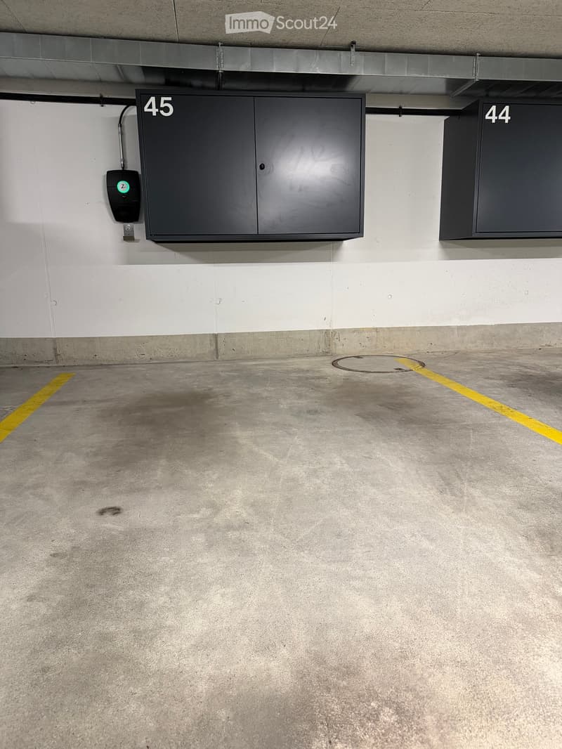 Underground parking garage with numbered storage cabinets and a charging station.