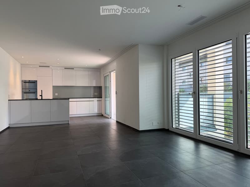 Modern kitchen with white cabinets, stainless steel appliances, dark tiled floor, and large sliding glass doors leading to a balcony.