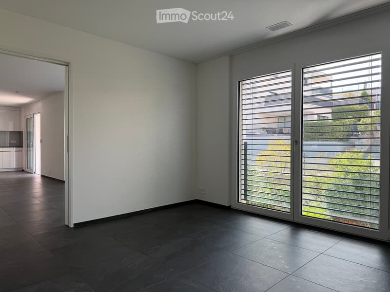 Empty room with dark tiled floor, white walls, large sliding glass doors with blinds, and an open doorway leading to another room.