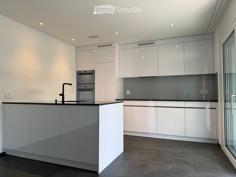 Modern kitchen with white cabinets, a central island, and built-in appliances including an oven and sink.