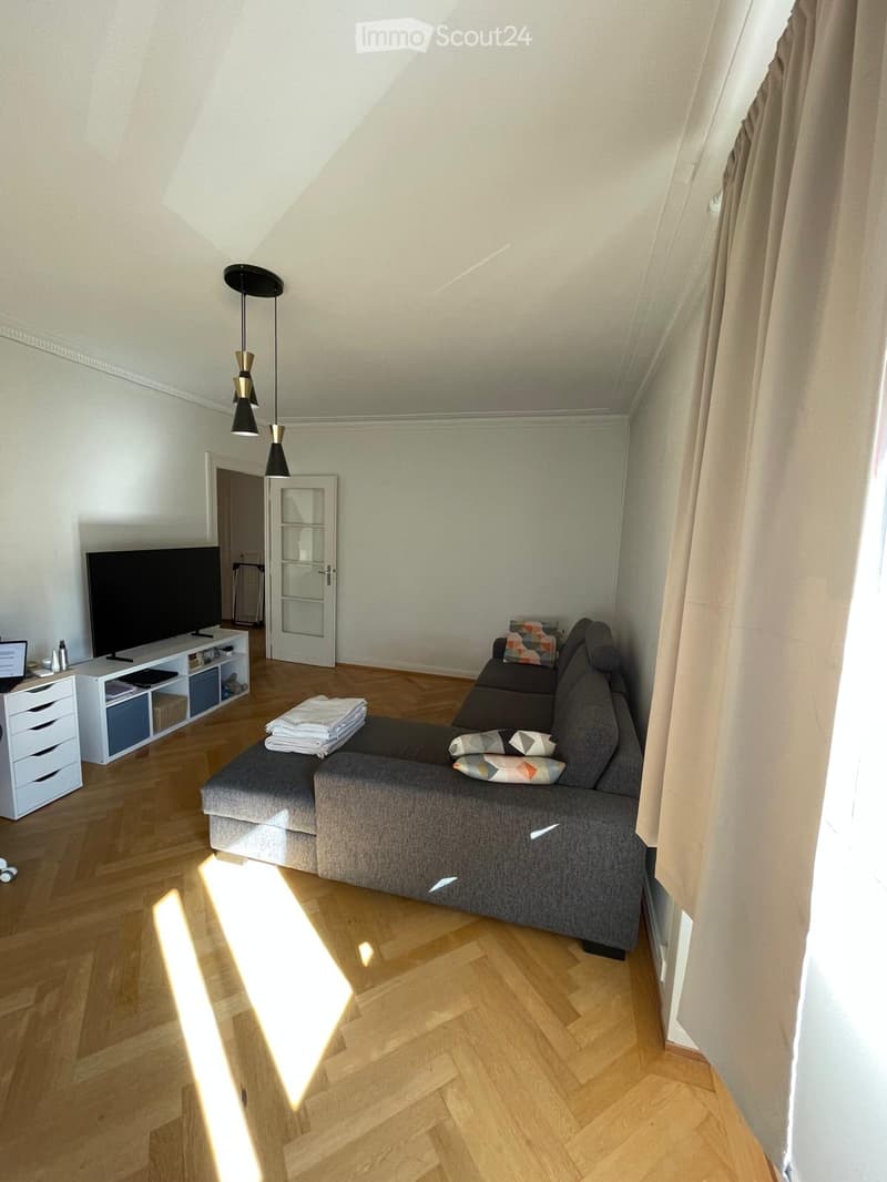 Living room with wooden flooring, grey sectional sofa, coffee table, TV, drawer unit, and floor lamp.