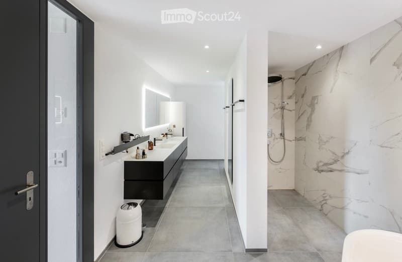 Modern bathroom with a double sink, sleek black vanity, marble shower area, and built-in storage. Features include a large mirror, modern fixtures, and recessed lighting.