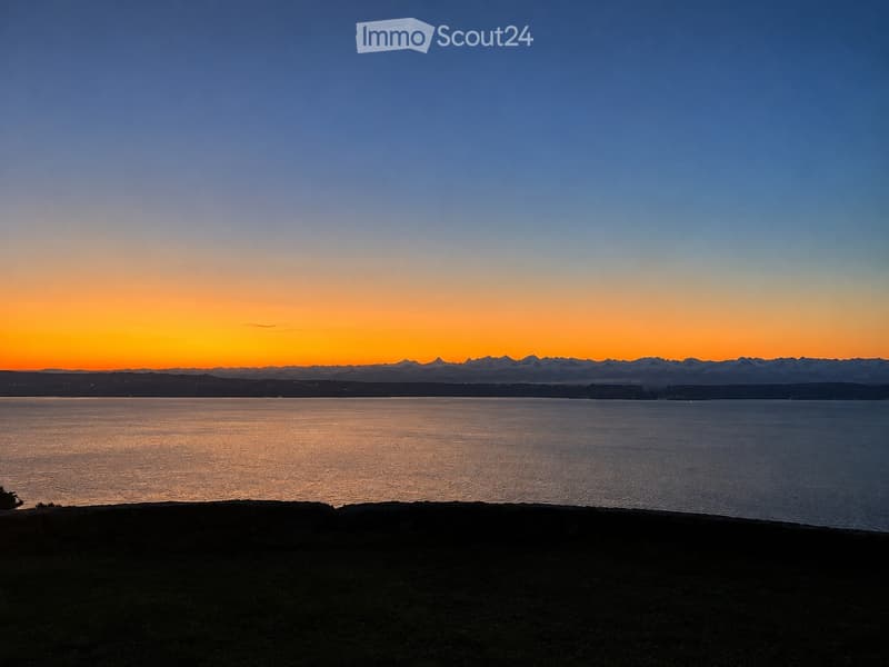 A serene view of a body of water at sunset, with distant mountains and a gradient sky transitioning from deep blue to warm orange hues.