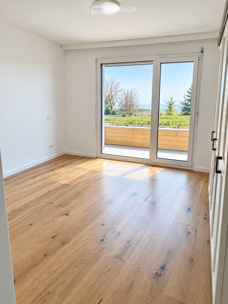 Empty room with light wooden flooring, white walls, and large sliding glass doors leading to a garden with a scenic view.