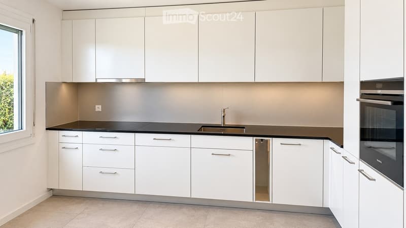 Modern kitchen with white cabinets, black countertops, and stainless steel appliances including a sink and oven.