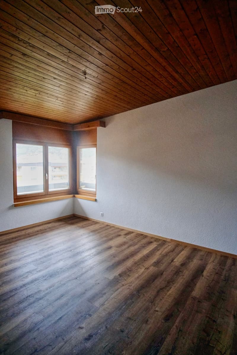 Empty room with wooden flooring, white walls, and wooden-framed windows letting in natural light.