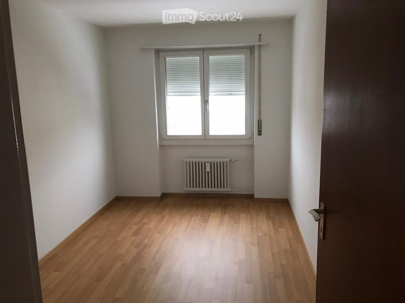 Empty room with wooden flooring, white walls, a window with blinds, and a radiator below the window.