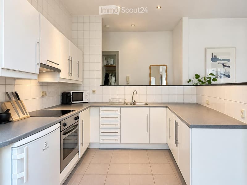 Modern kitchen with white cabinets, stainless steel appliances, and a central island. Features an oven, microwave, knife block, and a sink with a modern faucet.