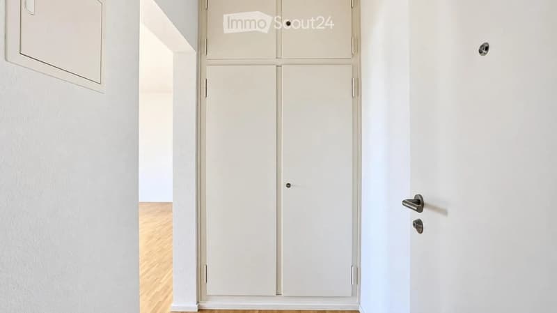 A clean, minimalist hallway with white walls, light wooden flooring, and a set of white double doors.