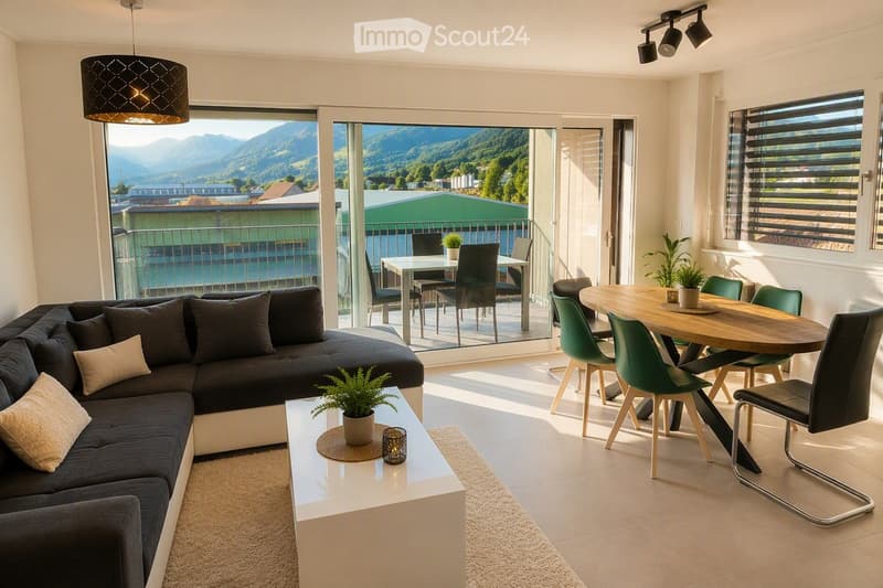 Modern living and dining area with large windows offering a scenic mountain view, featuring a dark grey sectional sofa, white coffee table, wooden dining table with green chairs, and decorative plants.