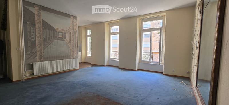 Empty room with beige walls, blue carpet, large windows, and a mural on one wall.